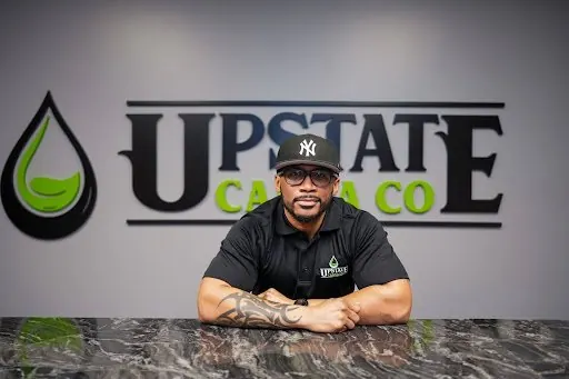 Upstate Canna Co. team member seated at the counter under the logo
