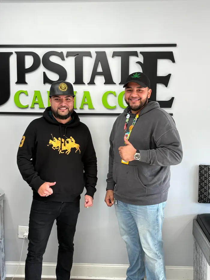 Two Upstate Canna Co. team members in front of the logo wall